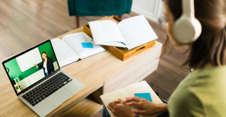 Elevă care participă la o oră de meditații online, urmărind explicațiile profesoarei pe laptop